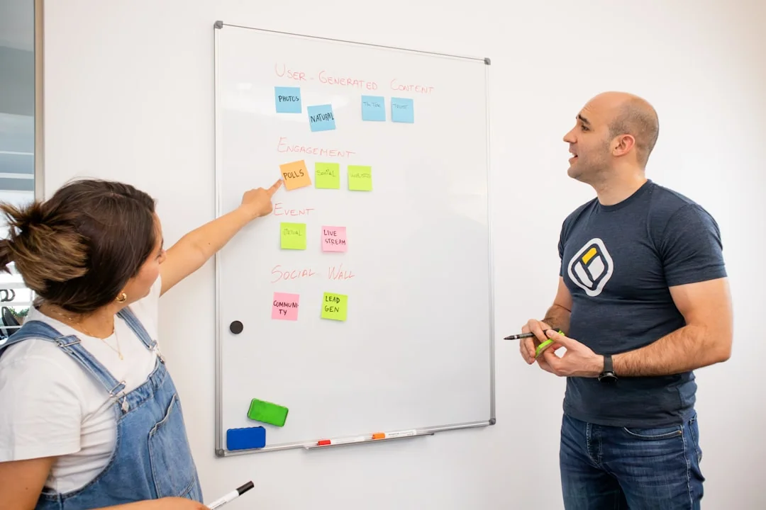 Two colleagues collaborate on a marketing strategy using a whiteboard, focusing on user-generated content.